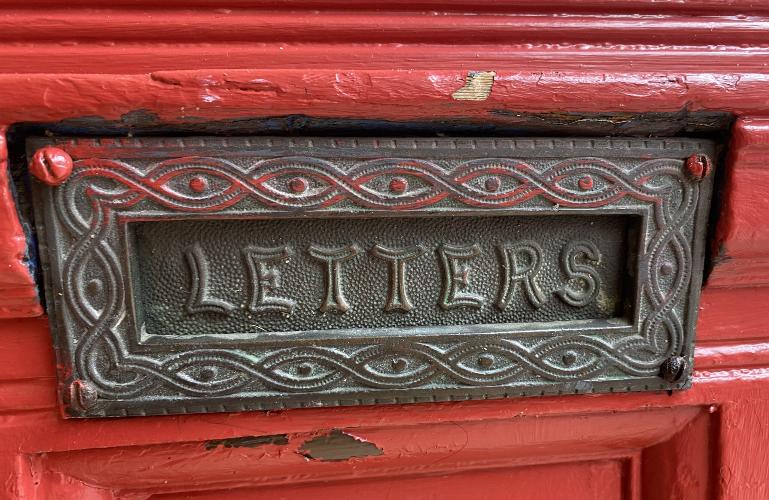 An ornate, grey metal letter box on a cherry red wooden door, with the word 'LETTERS' on it. 